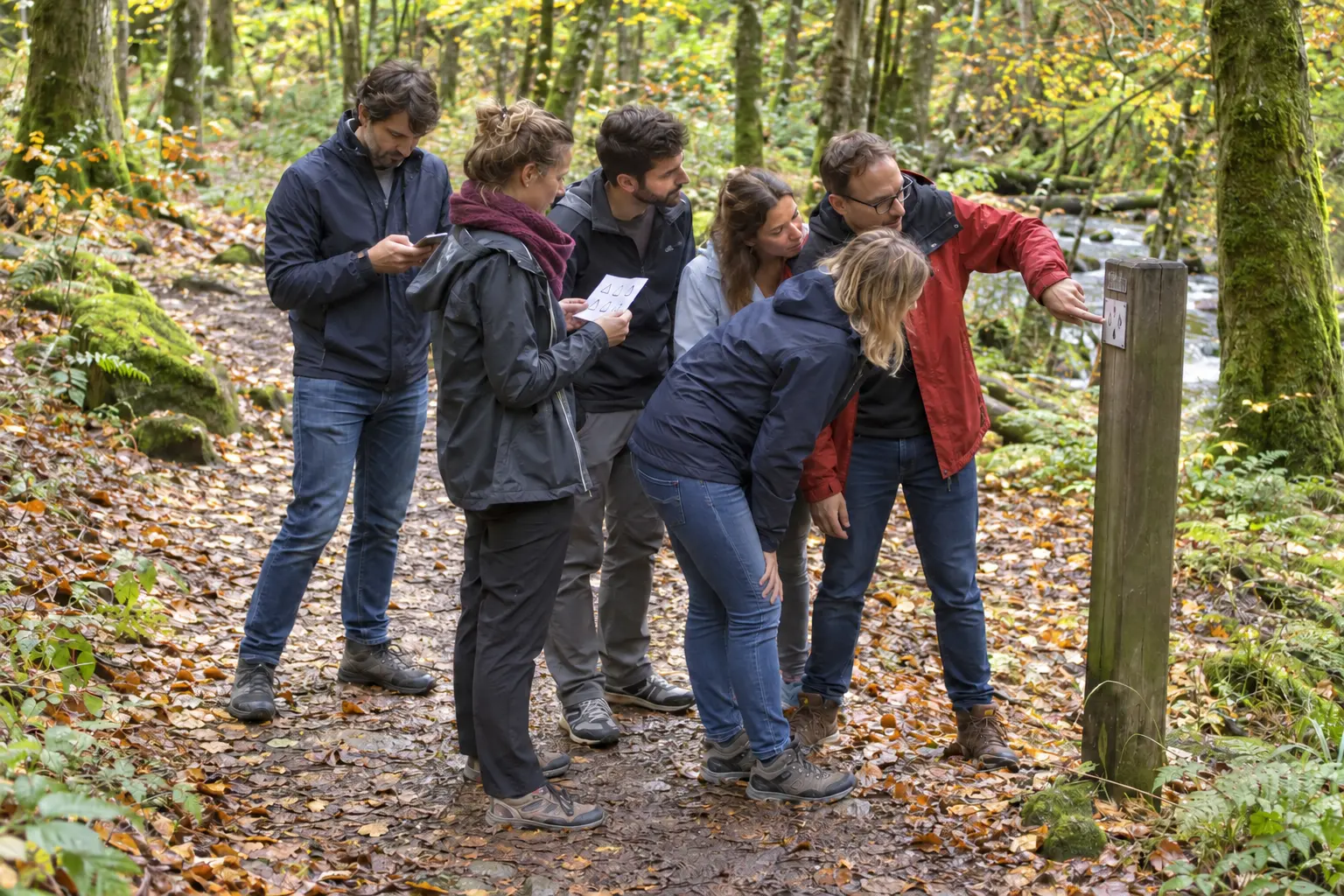 Groupe de collègues rassemblés autour d’un indice en forêt, comparant leurs observations pendant un défi de déduction.