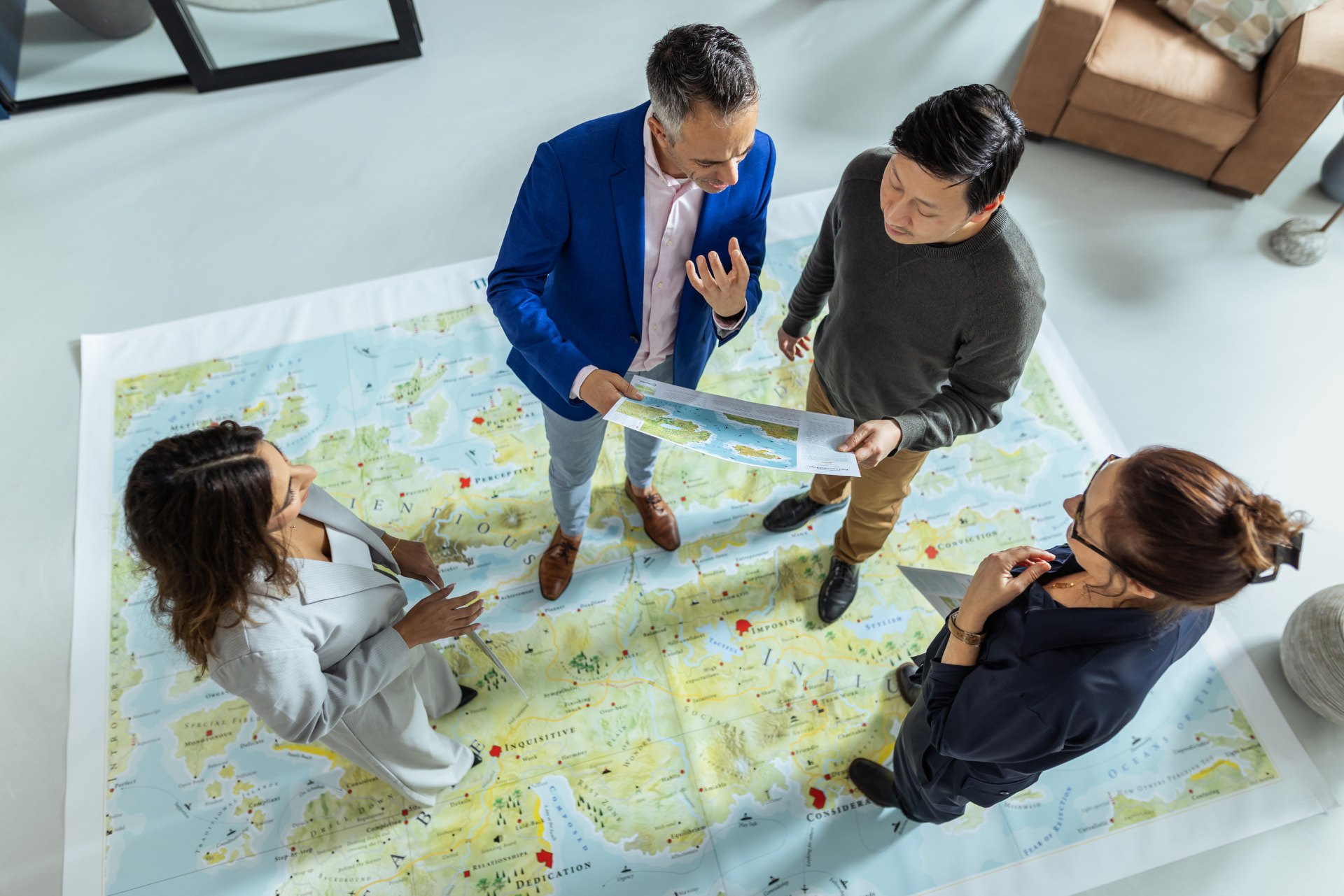 Quatre personnes échangent debout autour d’une grande carte Mapstell® déployée au sol dans une salle claire.